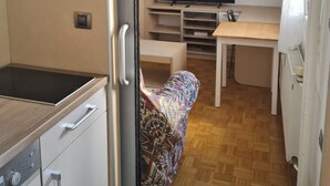 A compact kitchenette with a stove, microwave, and cabinets. There is a TV on a stand and a patterned chair. - Studio Beni (Ljubljana)