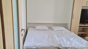 A bedroom with a bed, wooden wardrobe, and a television. - Studio Beni (Ljubljana)