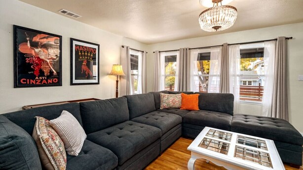 A living room with a sectional sofa, a white coffee table, and two posters on the wall. - Vintage Vine House Retreat~ walk to Main St! (Murphys)