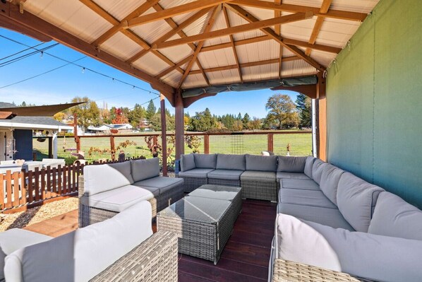 Un espacio de estar al aire libre cubierto con un amplio sofá modular, una mesita y una estructura de pérgola.