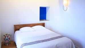 A bedroom with a wooden headboard, a bed with white linens, a small bedside table, a wall-mounted light, and a blue door frame.