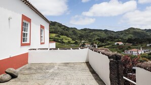 A white building with red trim and a balcony overlooking a green landscape with hills.