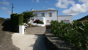 A white building with red trim and a tiled roof, a paved entrance, and a stone wall.