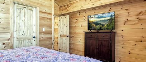 A wooden cabin bedroom with a bed, a dresser, and a painting of a mountain landscape.