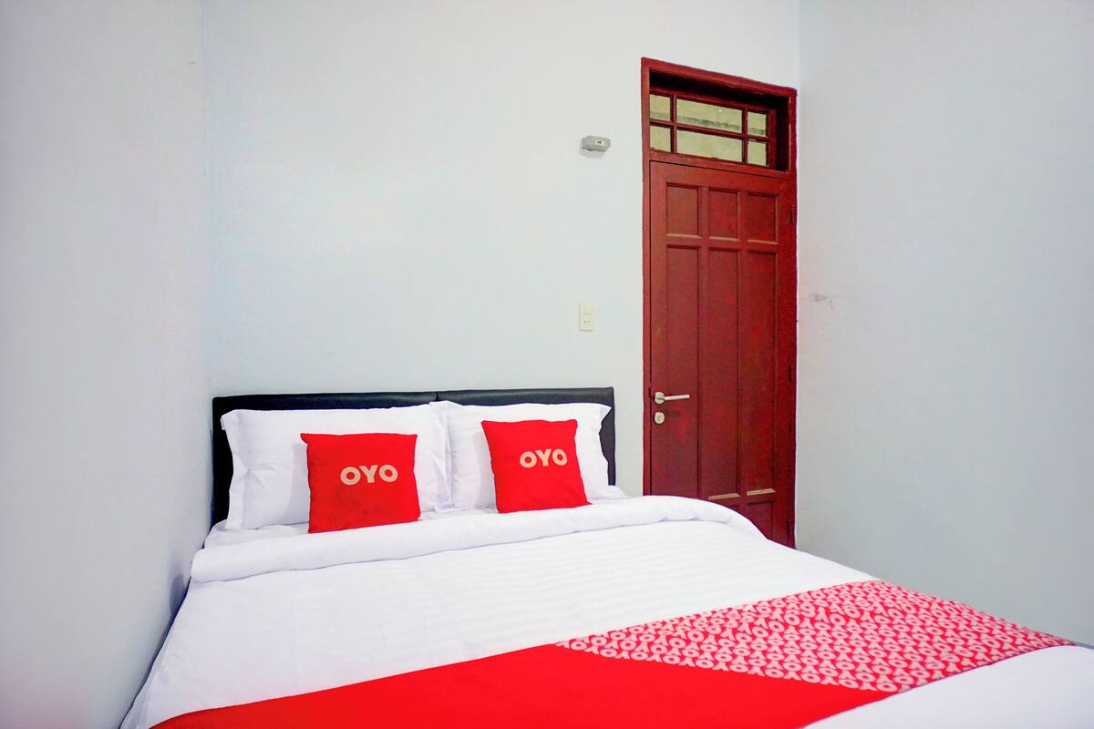 A bed with white bedding and red pillows, a red door, and a white wall.