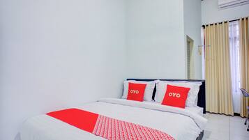 A hotel room with a bed, two pillows with the word 'OYO' on them, a window with curtains, and an air conditioning unit on the wall.