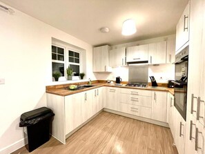 Une cuisine compacte avec des meubles de couleur bois clair, une hotte de cuisinière en acier inoxydable et une poubelle noire.