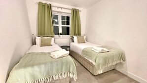 Un dormitorio con dos camas, una ventana con cortinas, una mesita redonda y una lámpara.