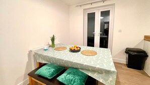 Un rincón comedor con una mesa dispuesta para dos, un radiador, un cubo de basura y una puerta que da a otra habitación.