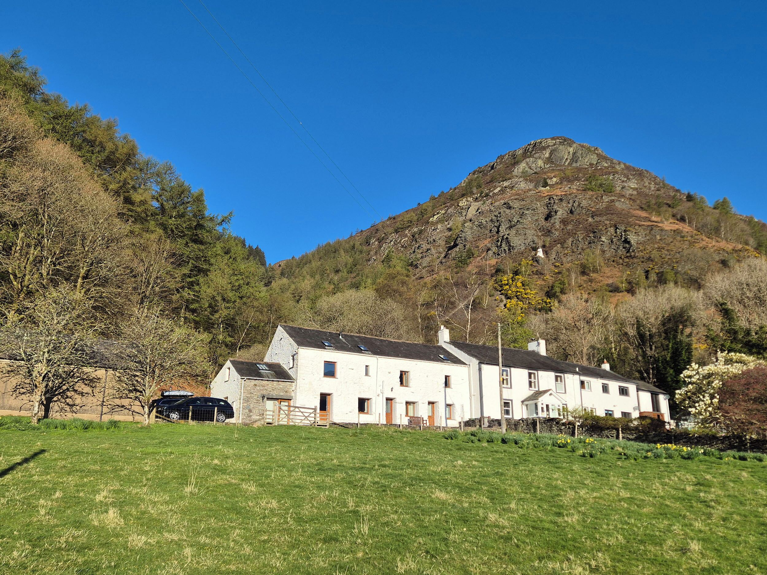 A white building with multiple windows and a sloped roof, situated in a grassy field with a mountain in the background.