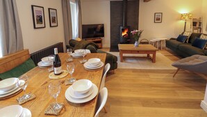 Un coin repas avec une table en bois dressée pour le repas, un canapé, un téléviseur et une cheminée.