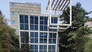 A modern building with a glass facade and a covered outdoor area with tiled flooring. - Sai Kan Hotel (Shirdi)