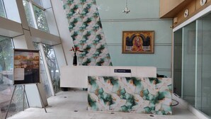 A reception desk with a floral pattern, a reception sign, and a framed religious icon on the wall. - Sai Kan Hotel (Shirdi)