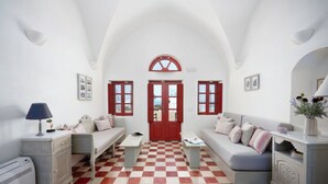 Una habitación con piso a cuadros, paredes blancas, una puerta roja y un sofá gris con almohadones.