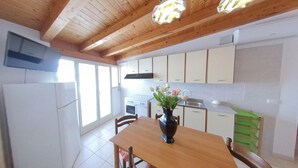 Una cocina con vigas de madera, armarios blancos, una mesa de comedor con sillas y un jarrón con flores.