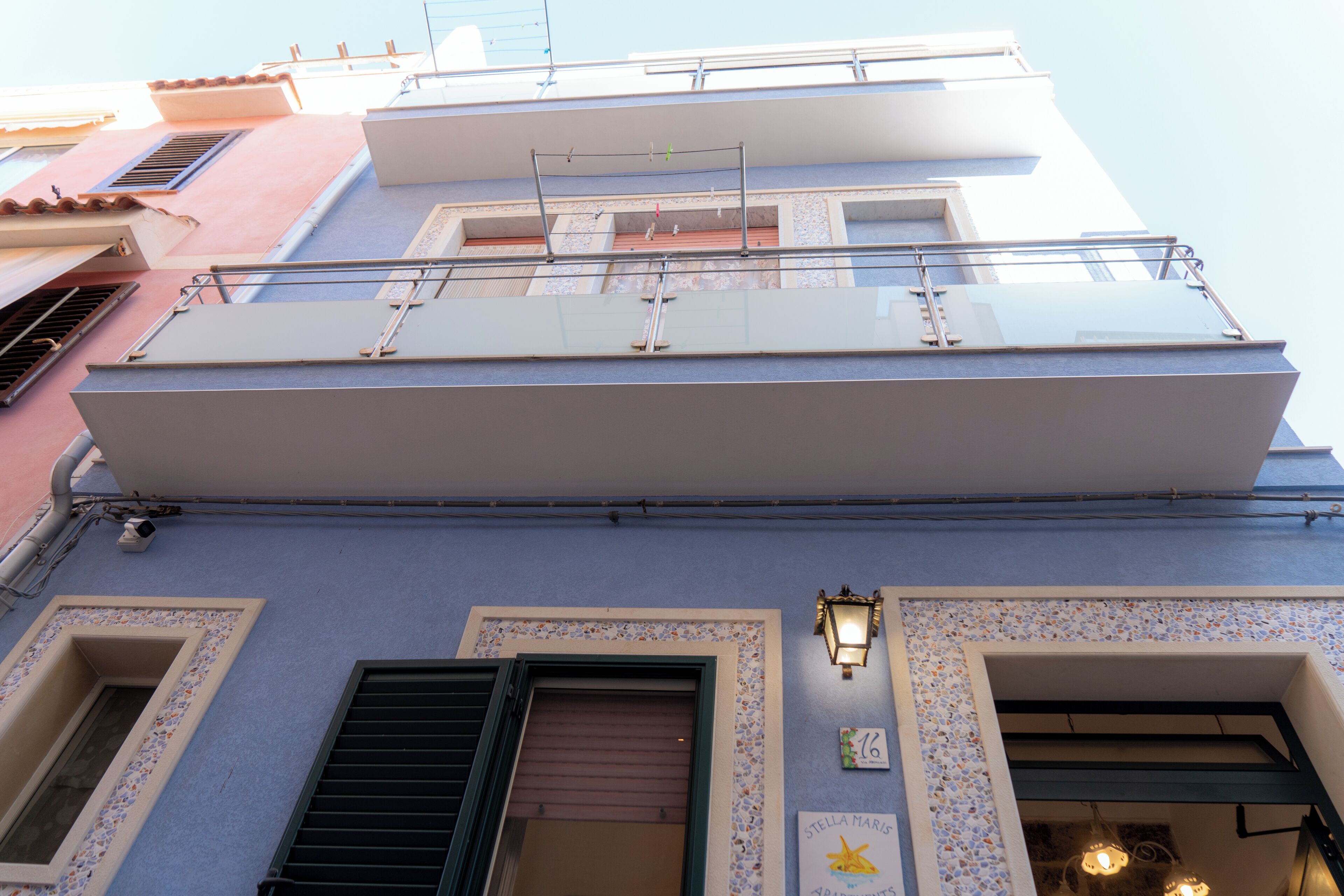 A multi-story building with balconies, a visible window with shutters, and a wall-mounted light fixture.