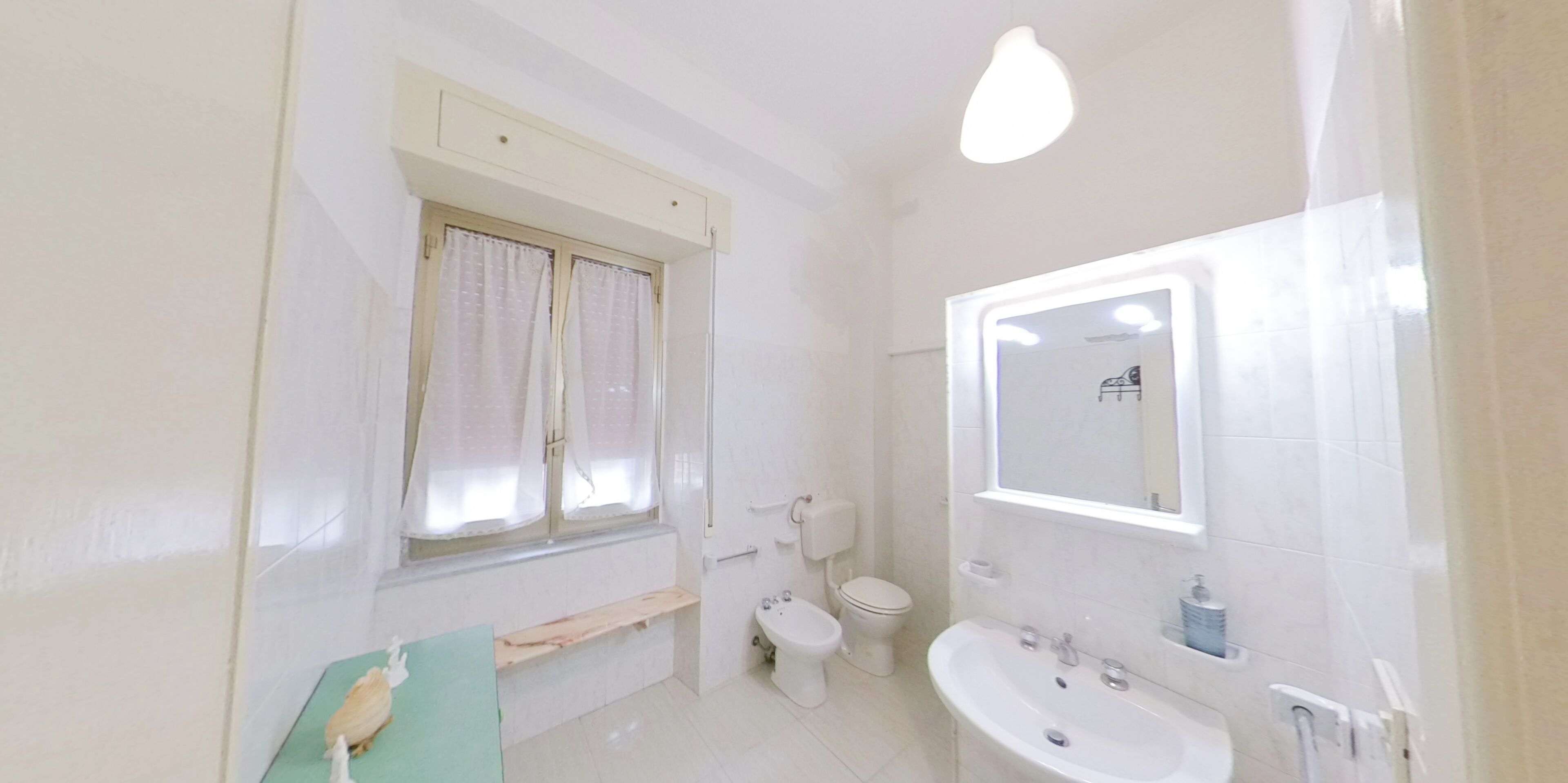 Une salle de bain avec des toilettes, un lavabo et une fenêtre avec des rideaux.