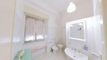 Une salle de bain avec des toilettes, un lavabo et une fenêtre avec des rideaux.