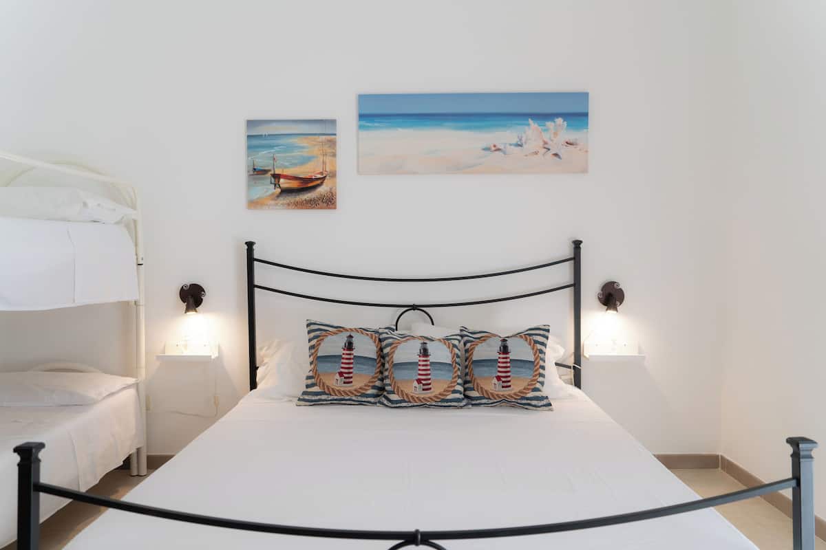 A neatly arranged bedroom with a single bed, two wall-mounted lamps, and two framed beach paintings.