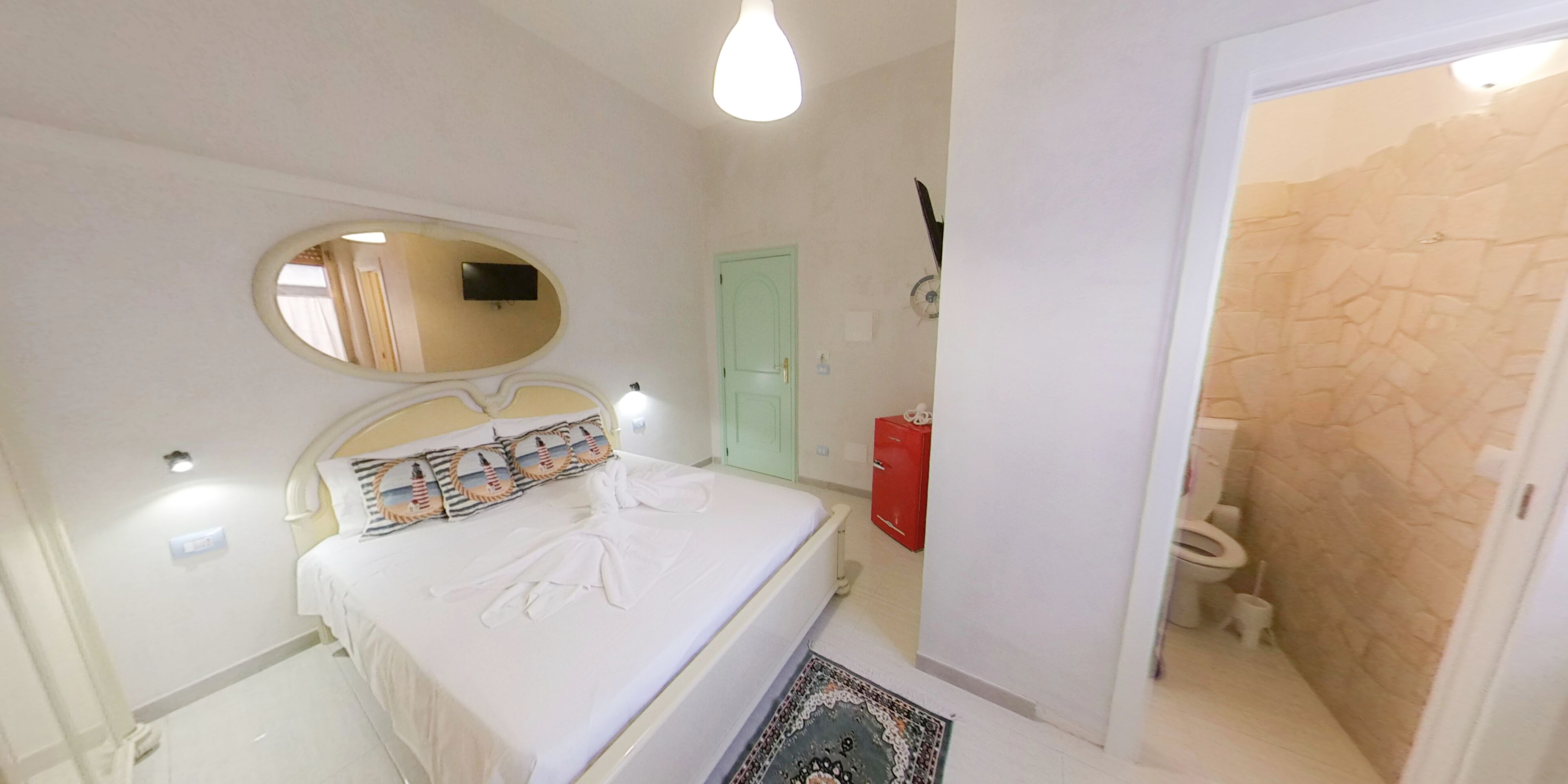 Ein Schlafzimmer mit Bett, Spiegel, einem roten Schrank und einem Badezimmer mit Toilette und Dusche.