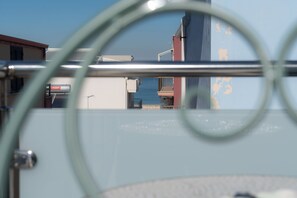 Vista a través de una ventana con barrotes, mostrando un edificio con puerta roja y cielo azul.