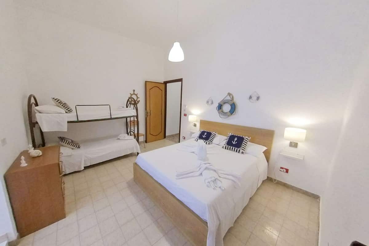 A hotel room with a single bed, a small desk, a chair, a wardrobe, and a door.