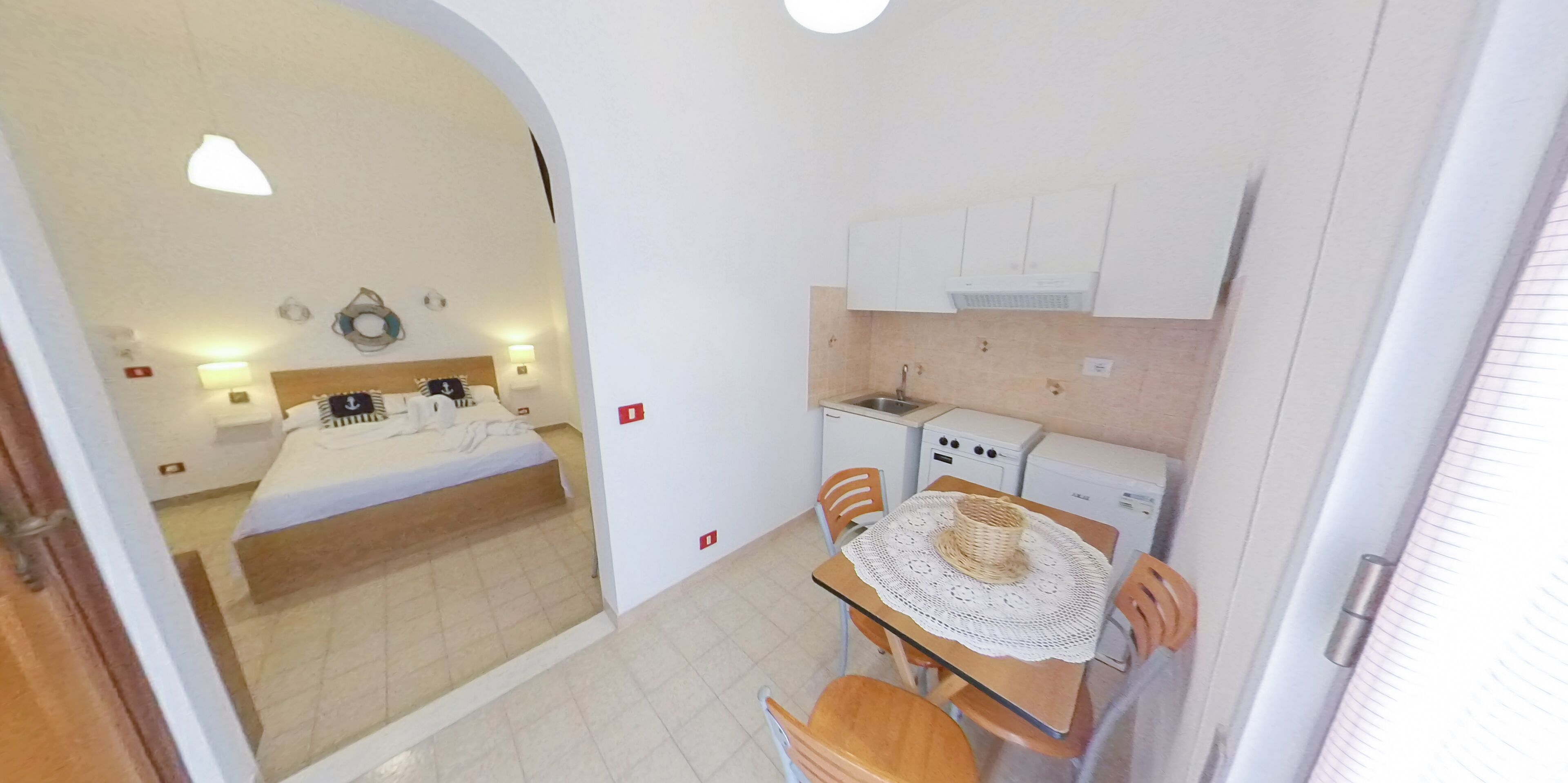 A compact hotel room with a bed, a small kitchenette, and a dining area with a table and chairs.