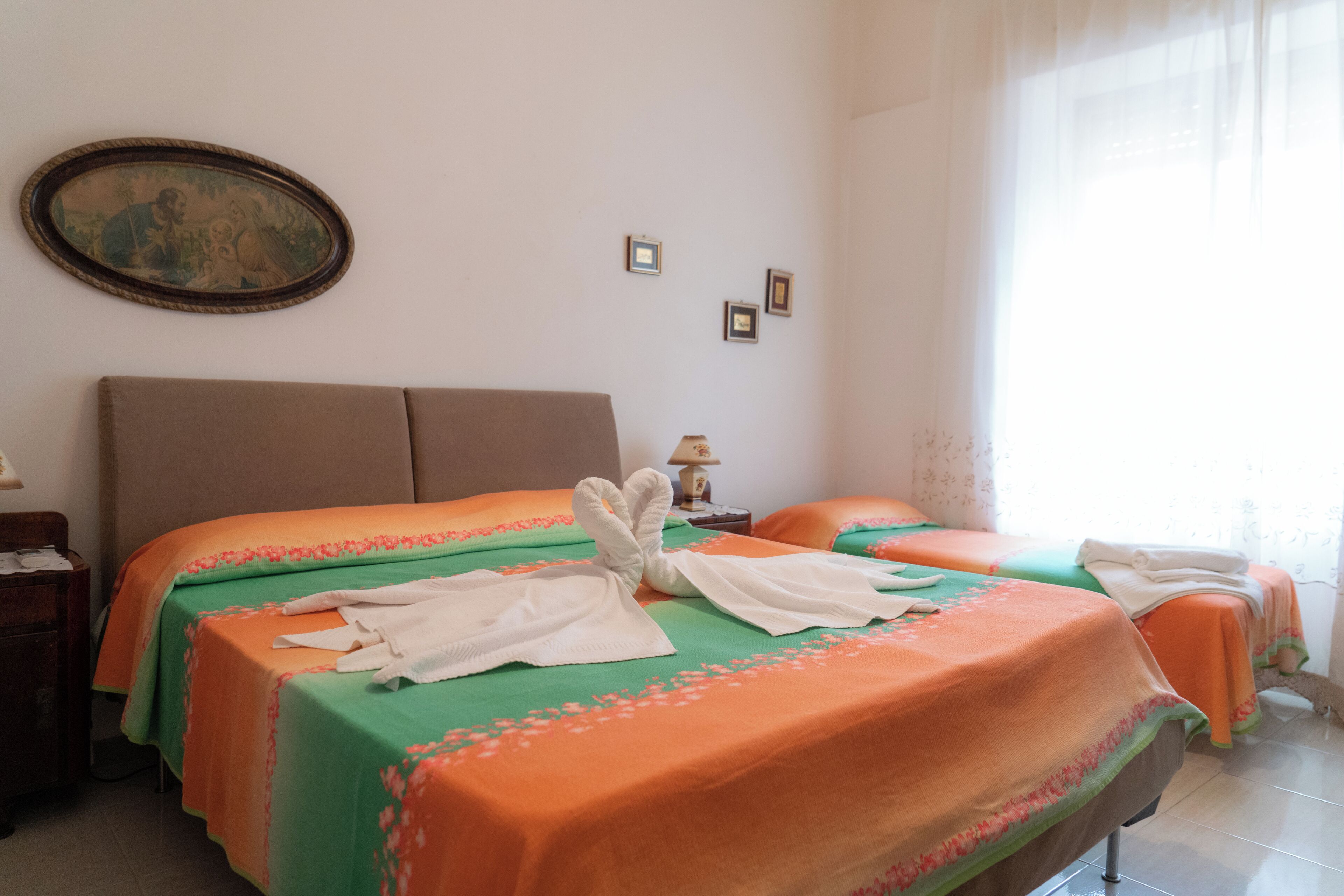 Une chambre d’hôtel avec deux lits, chacun recouvert d’une couverture verte et orange, et un tableau accroché au mur.