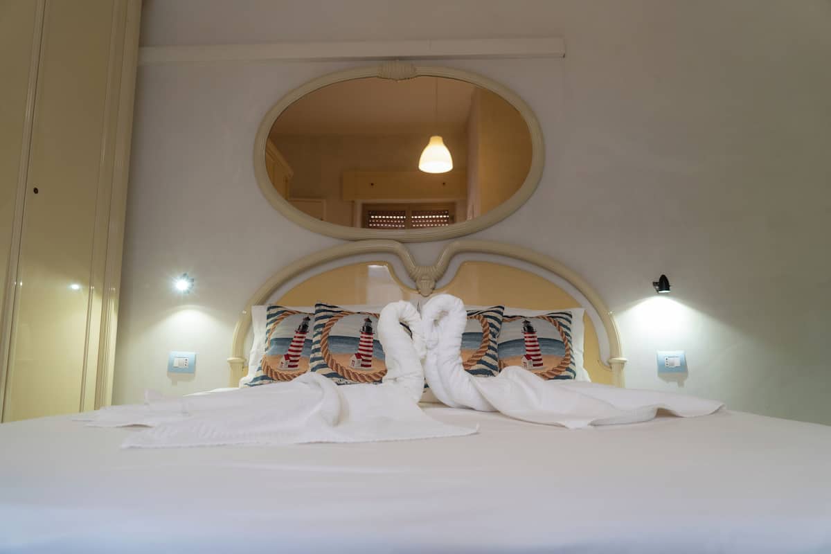 A hotel room with a large bed, a round mirror above the bed, and two wall-mounted lights.