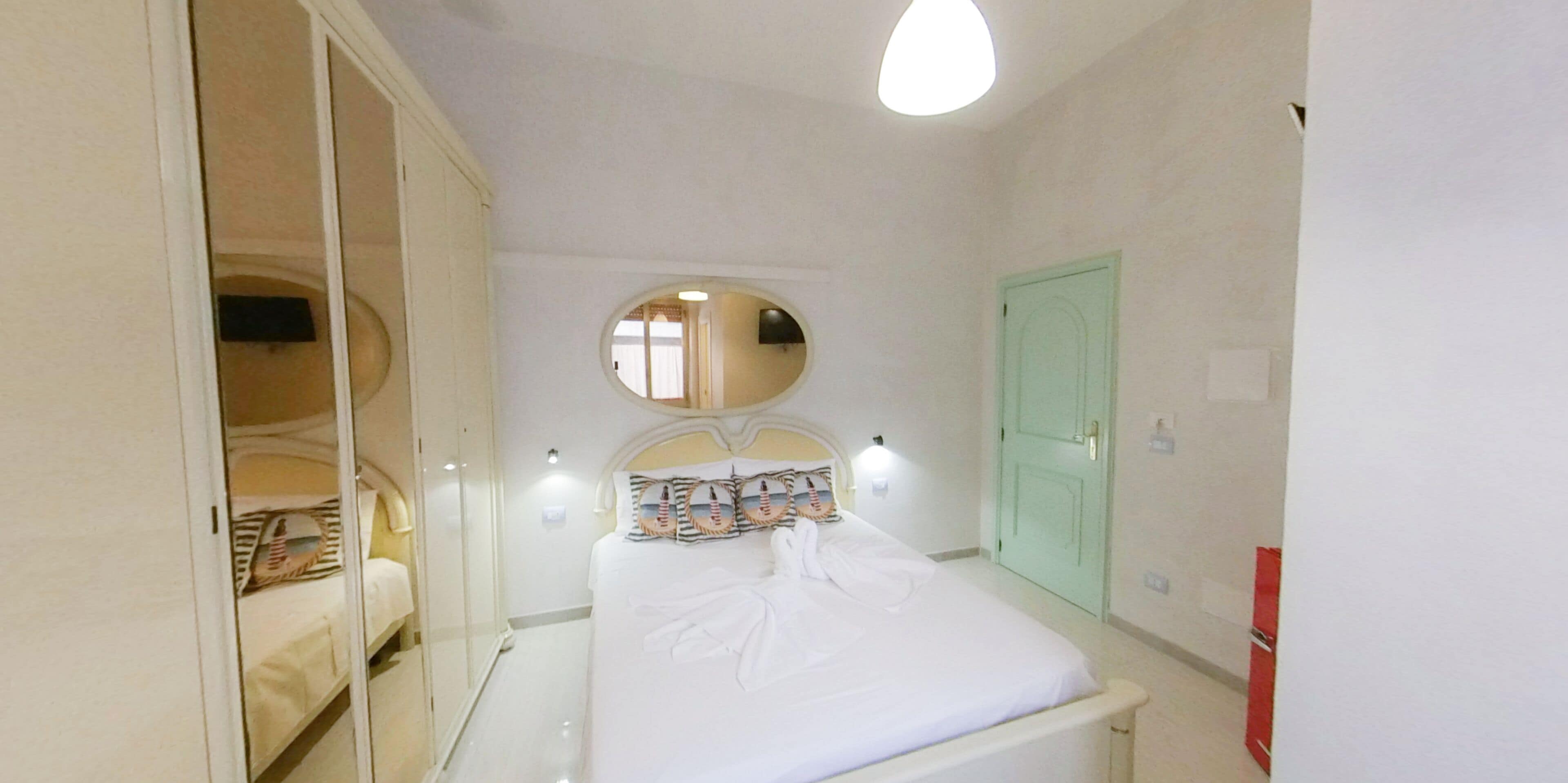 A bedroom with a bed, a wardrobe, a mirror, and a door.