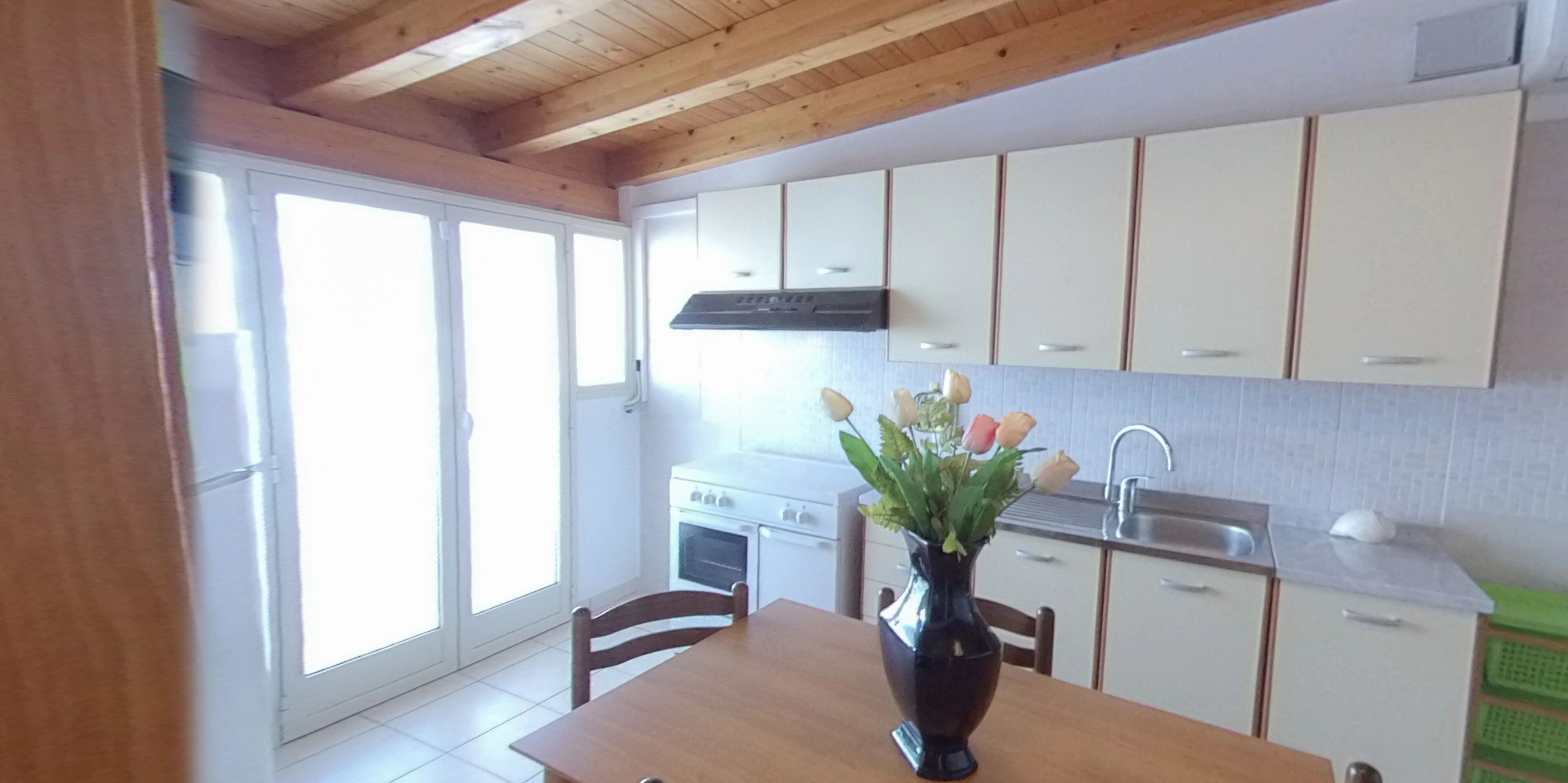 A kitchen with white cabinets, a stove, and a sink. There is a vase with flowers on the table.