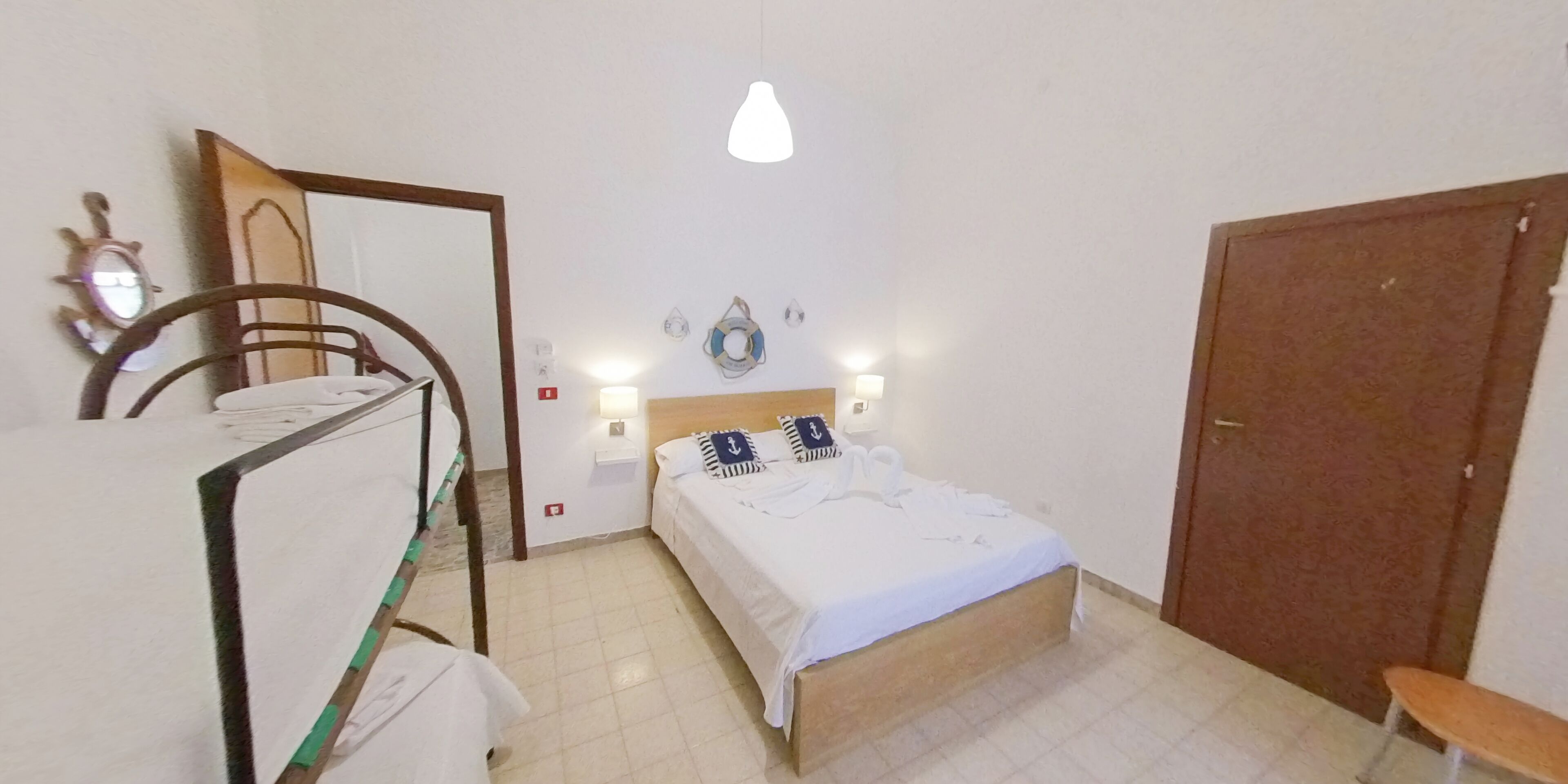 A bedroom with a bed, bedside tables, a hanging light fixture, a wooden door, and a bench.
