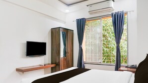 A hotel room with a bed, a TV mounted on the wall, a wardrobe, and a window with curtains.