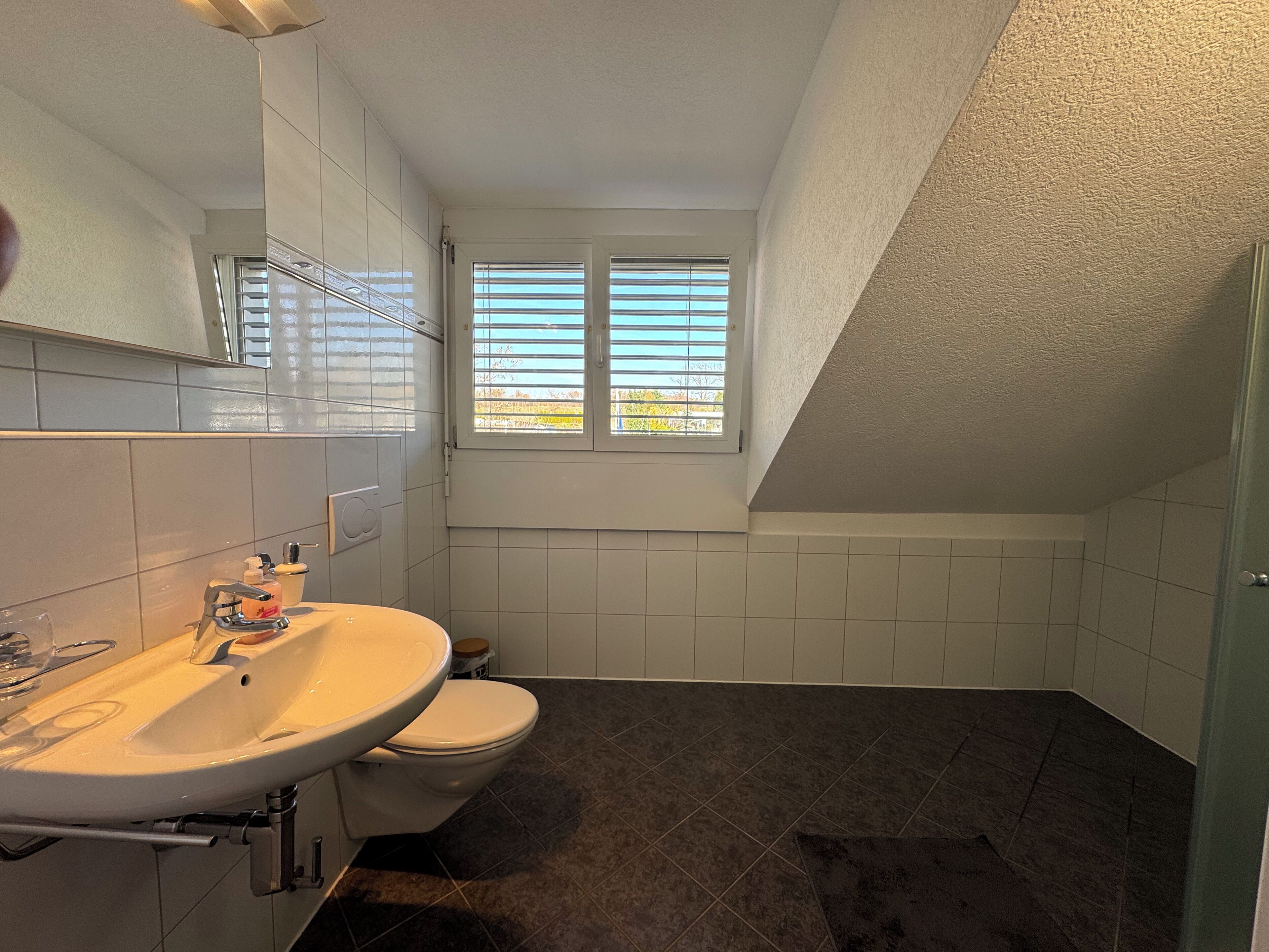 Un baño con lavamanos, inodoro y ventana con persianas.