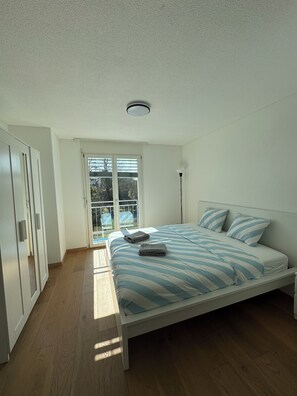 Un dormitorio con cama, armario, ventana y una lámpara en el techo.