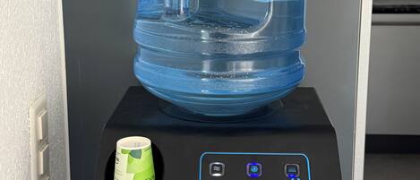 Un distributeur d’eau surmonté d’une grande cruche, accompagné d’un gobelet vert et doté d’un panneau de commande orné du logo de la marque.