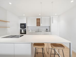 Une cuisine moderne avec des meubles blancs, un îlot central, deux tabourets de bar et des luminaires suspendus.