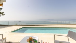 A pool with a clear view of the sea, two chairs, and a hat on a table. - Seafront House, 4 Bdr, 3 Bth, 9 Guests, Parking (Roses)