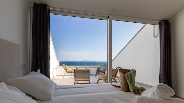 A hotel room with a bed, two chairs, a small table, and a view of the sea. - Seafront House, 4 Bdr, 3 Bth, 9 Guests, Parking (Roses)