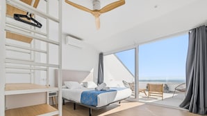 A modern hotel room with a bed, a ceiling fan, a balcony with chairs, and a view of the sea. - Seafront House, 4 Bdr, 3 Bth, 9 Guests, Parking (Roses)