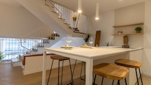 A modern kitchen with a white island, bar stools, and a staircase leading to an upper level. - Seafront House, 4 Bdr, 3 Bth, 9 Guests, Parking (Roses)