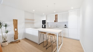 A modern kitchen with white cabinetry, a central island with stools, a built-in oven, and a refrigerator. - Seafront House, 4 Bdr, 3 Bth, 9 Guests, Parking (Roses)