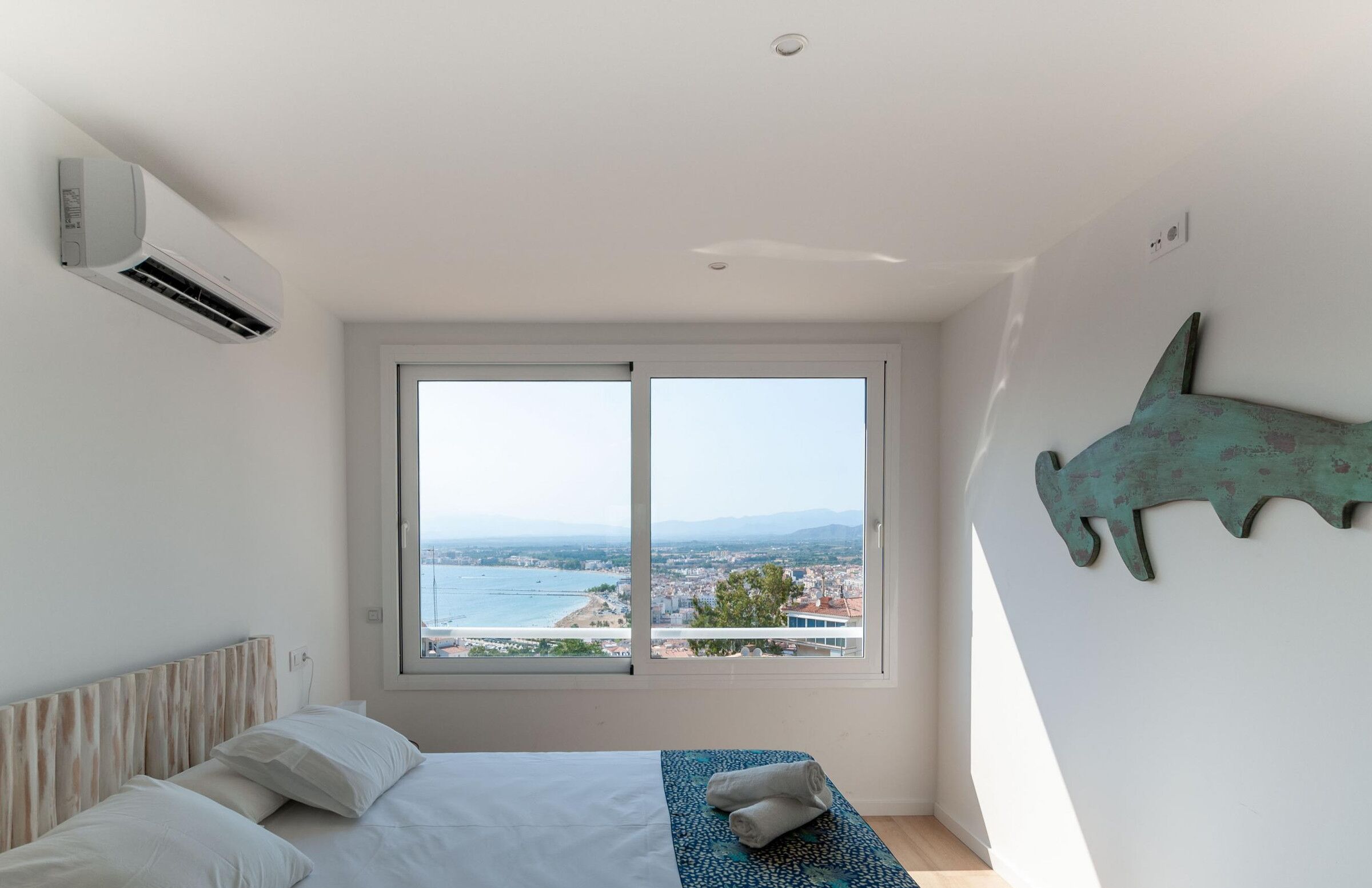 A bedroom with a large window, a bed, and a wall-mounted air conditioner.