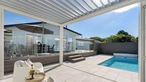 Un espacio al aire libre techado con piscina, asientos y vista a una casa.