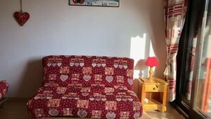 A cozy room with a patterned sofa, a small wooden side table with a lamp, and a window with curtains.