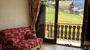 A room with a patterned sofa, a wooden floor, and a view of a rural landscape through a glass door.