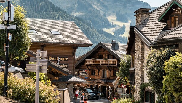 A mountain village with wooden buildings, a sign for 'Boulanger', and a view of the mountains.