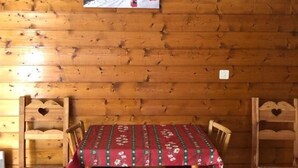 A wooden cabin interior with a dining table set for four, surrounded by wooden chairs with heart-shaped cutouts.