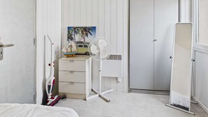 A bedroom with a bed, a dresser, a fan, a door, and a painting.