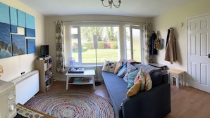 Una sala de estar acogedora con un sofá, un televisor, una estantería y un gran ventanal con vistas al exterior.